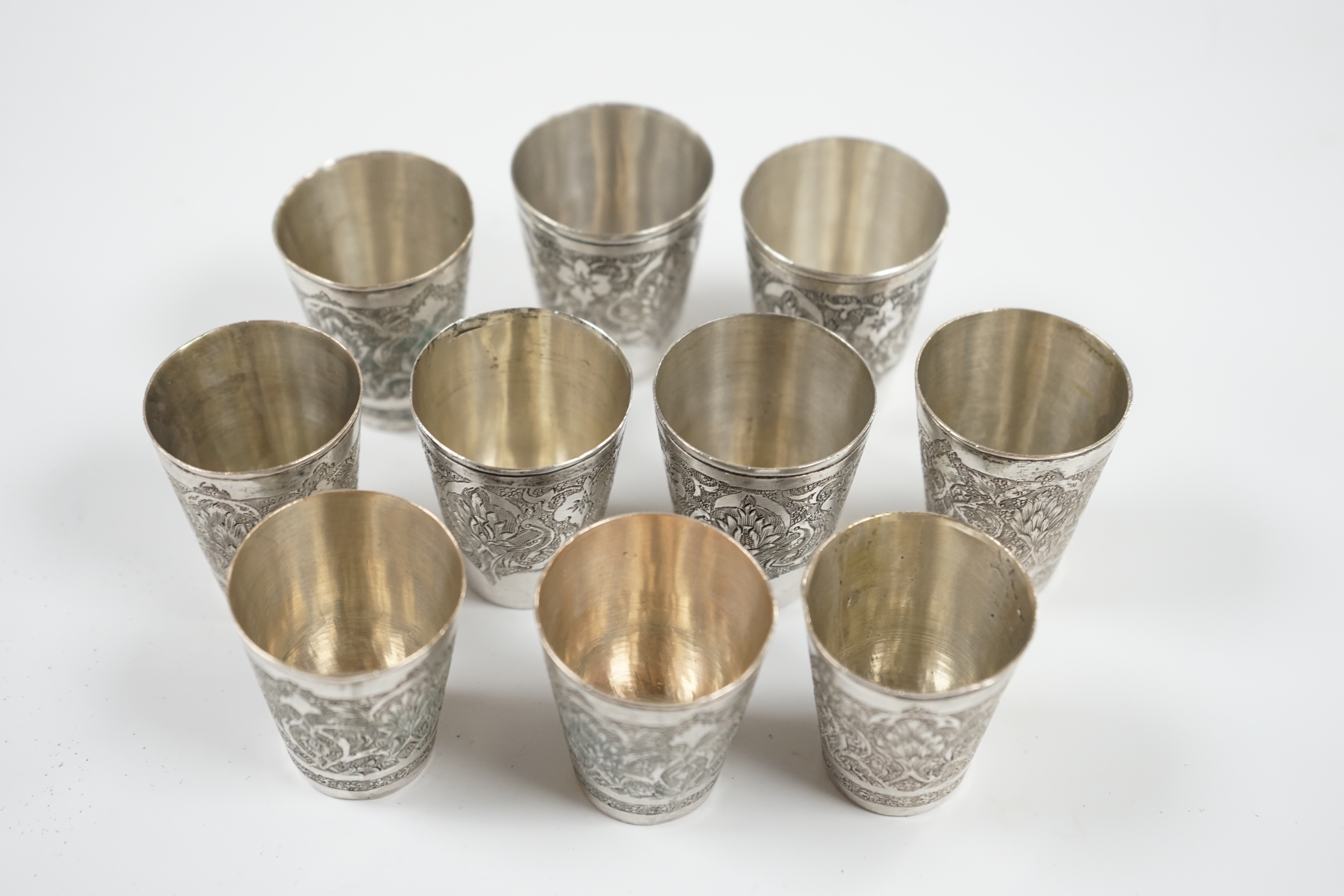 A set of four Persian engraved white metal tot cups, 43mm, stamped marks to the base and six other similar tot cups, 44mm, 8.7oz. Condition - fair